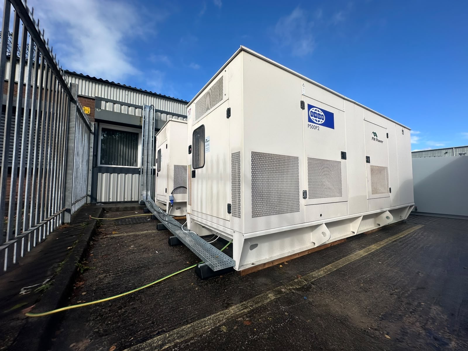 Two enclosed diesel generators installed beside the Fire Glass North building, with FG Wilson P500P2 and FW Power branding visible.