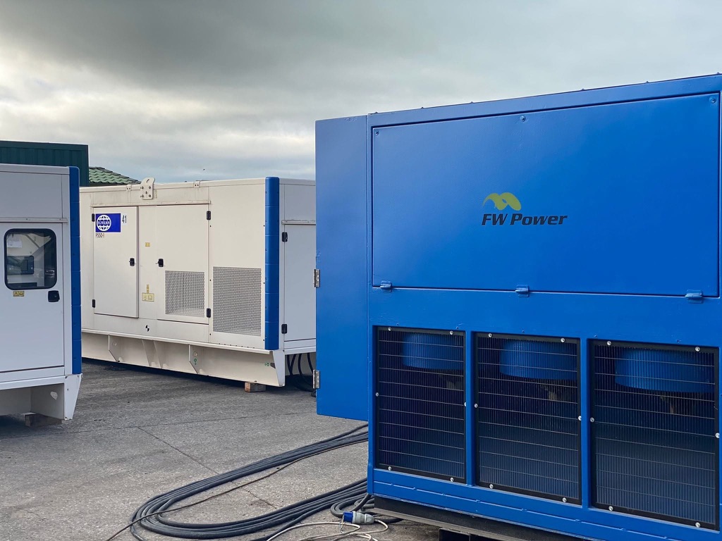 Blue FW Power diesel generator beside white acoustic generators and power cables in the workshop yard